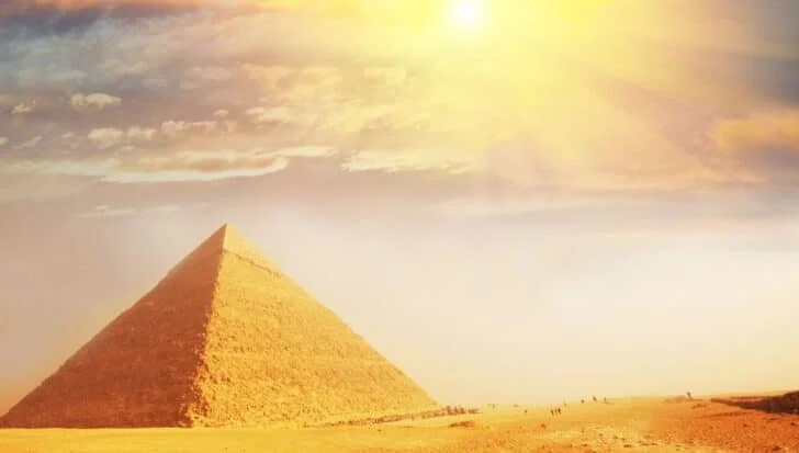 The Great Pyramid of Giza under a bright sun with a few people visible in the distance