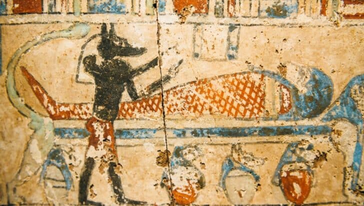 Ancient Egyptian wall painting depicting a funerary scene with Anubis, the jackal-headed deity, overseeing a mummified figure on a platform