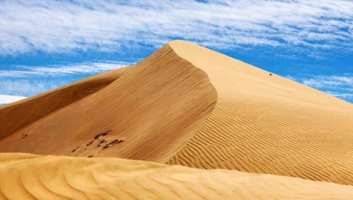 A large, textured sand dune under a blue sky