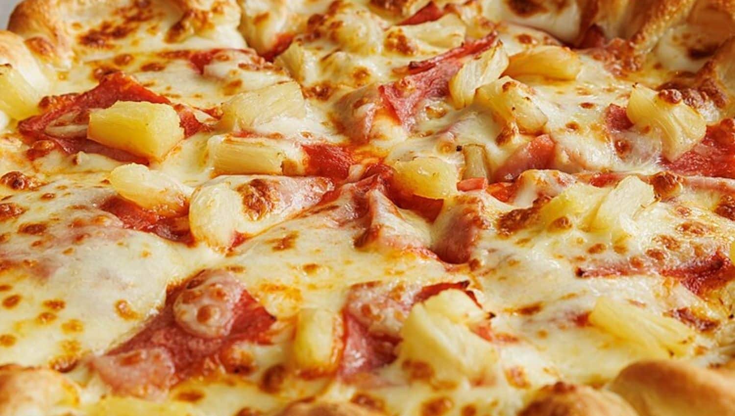 Close-up of a pizza topped with melted cheese, pineapple chunks, and slices of ham