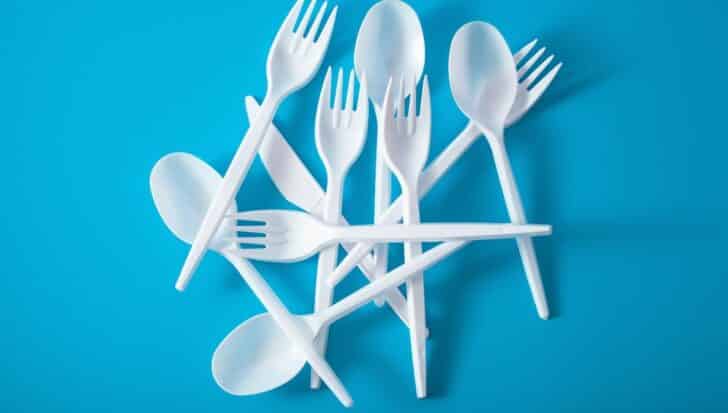 White plastic utensils including forks, spoons, and a knife on a blue background, illustrating single-use plastic items