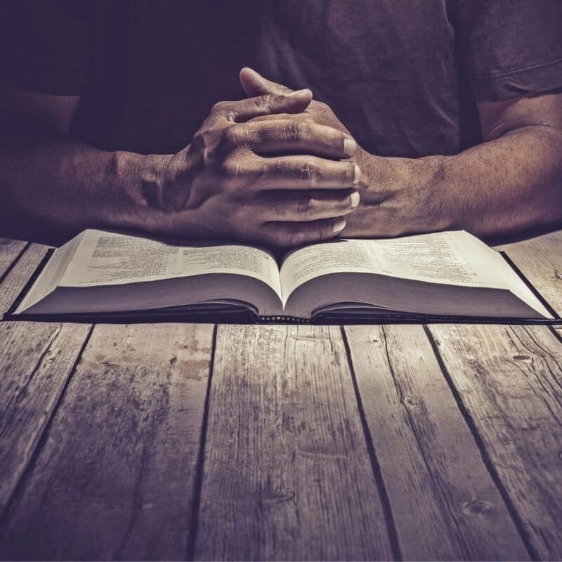 Hands clasped in prayer over an open Bible on a wooden table