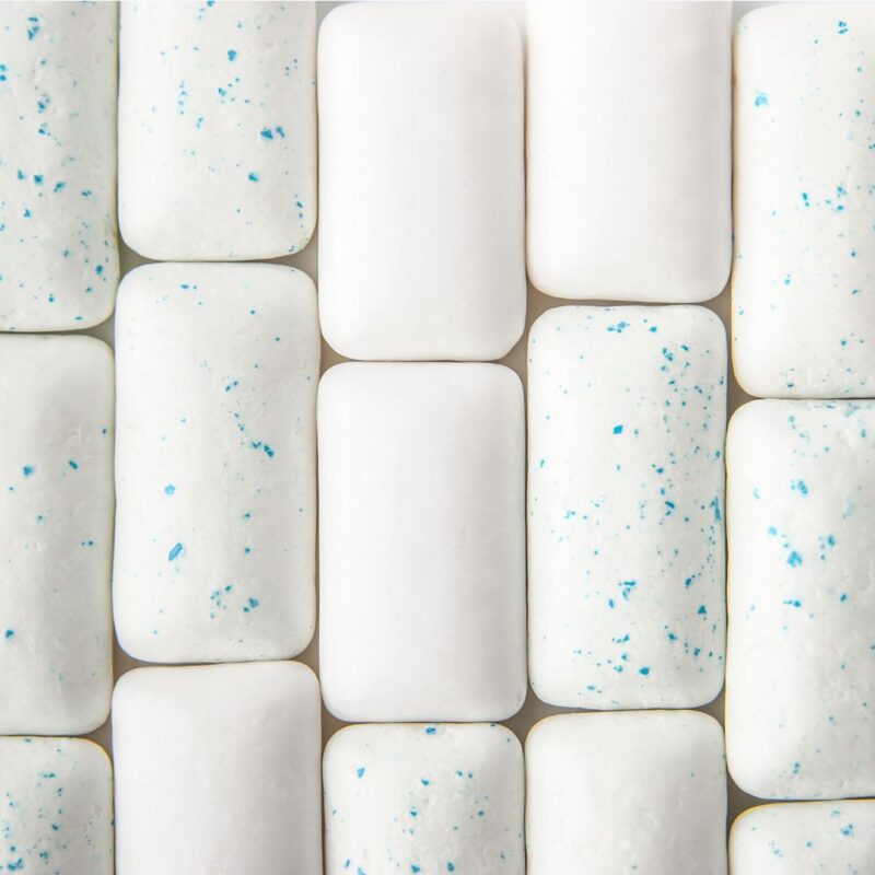 Close-up view of several rectangular white chewing gum pieces, some with blue speckles