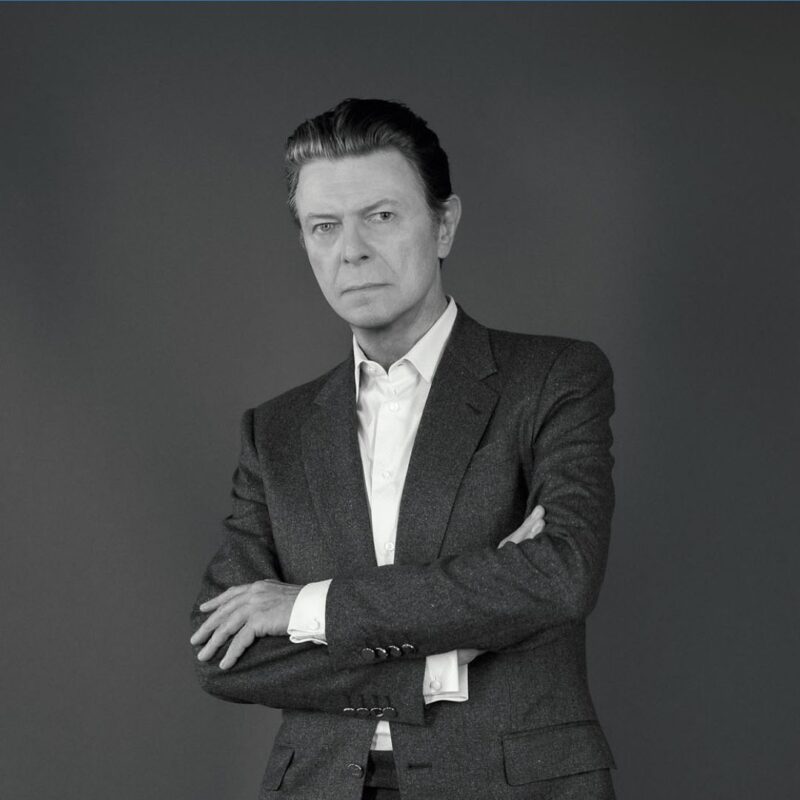 David Bowie in a suit with arms crossed against a plain background