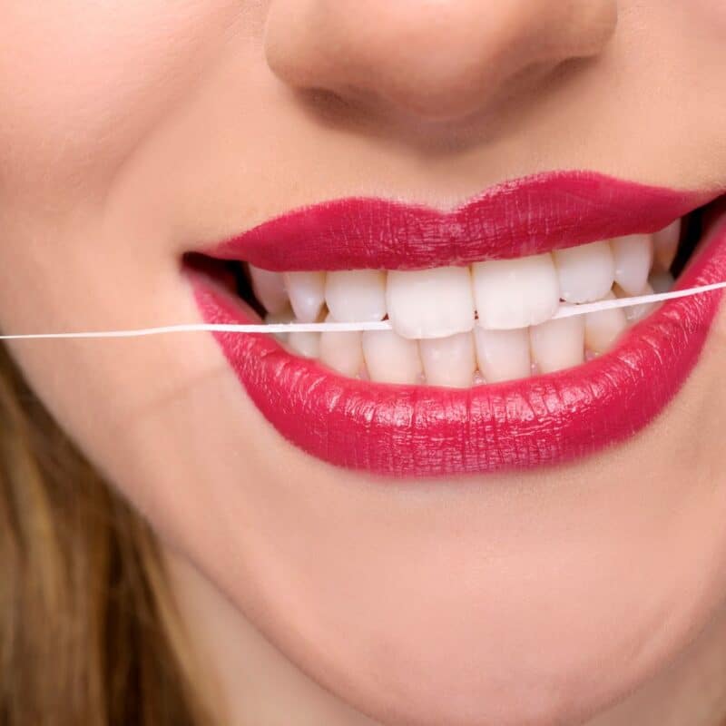 Close-up of a mouth with red lipstick and a piece of floss between white teeth