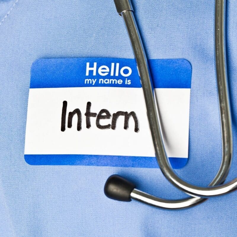 A stethoscope is draped over a blue medical uniform with a name tag reading 'Hello my name is Intern'