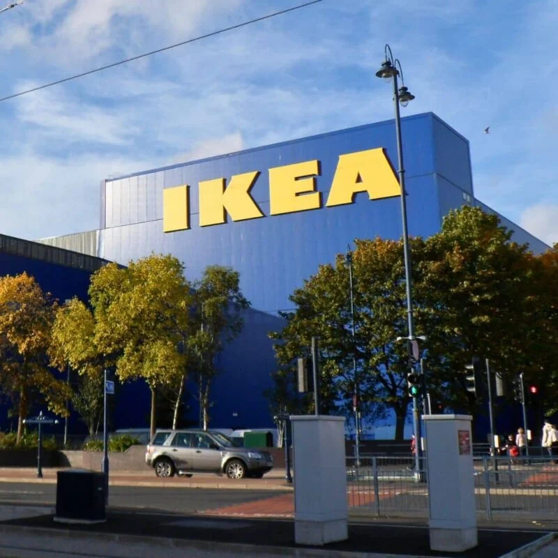 Large blue IKEA building, surrounded by trees and a parked silver car in front