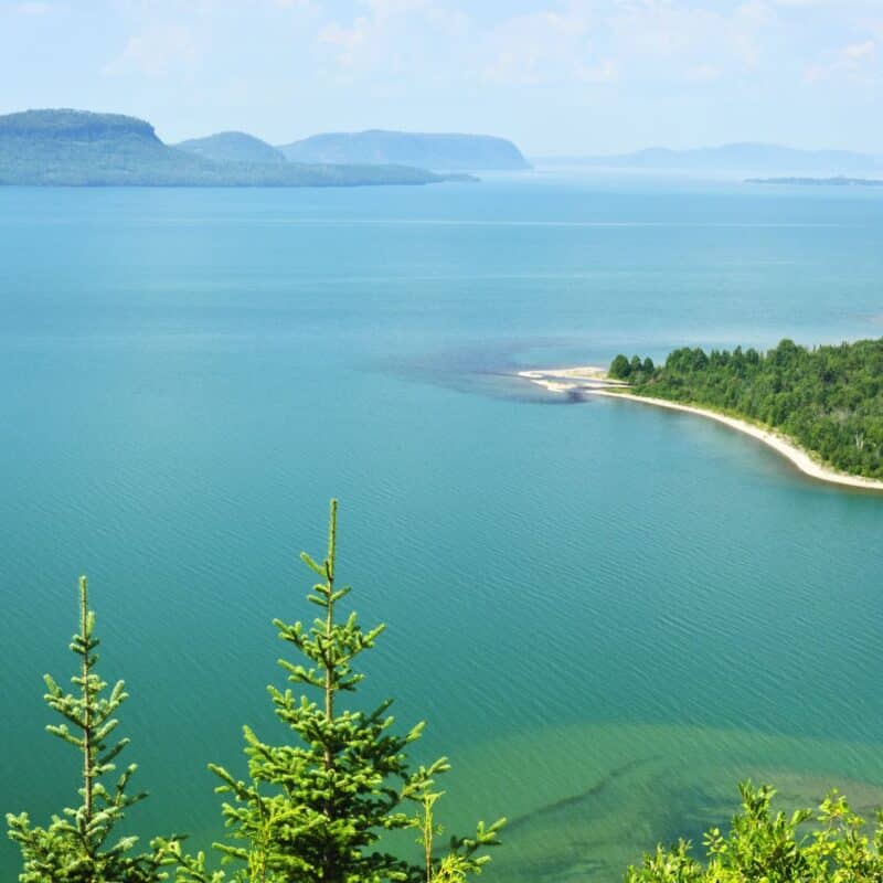 Expansive view of Lake Superior with clear blue water, lush green shoreline, and distant hills