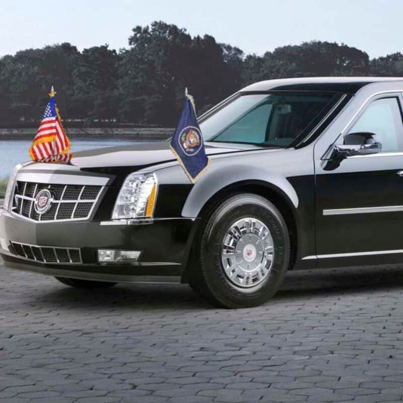 Presidential car with American flags on the front, black in color, parked on a cobblestone surface