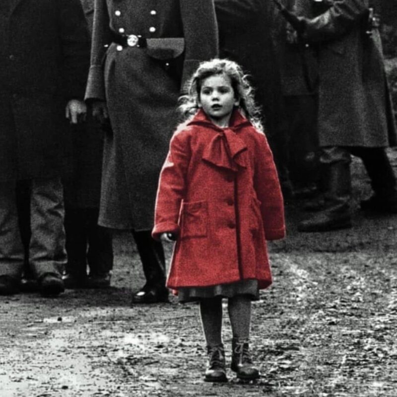 A young girl in a red coat stands out in an otherwise black and white scene, surrounded by adults in dark clothing