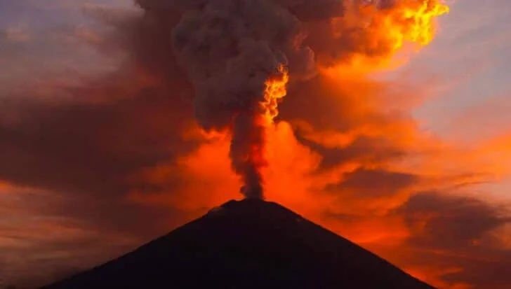 Volcano erupting with a plume of smoke rising against a colorful sky, illustrating active volcanic activity