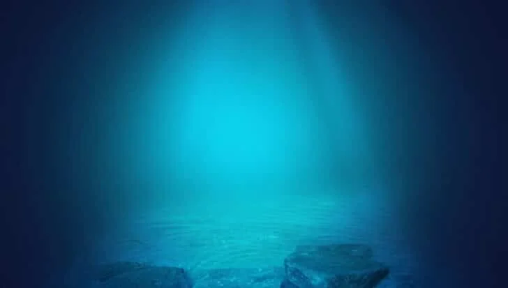 Underwater view with rocks on the seabed and blue water illuminated by light.