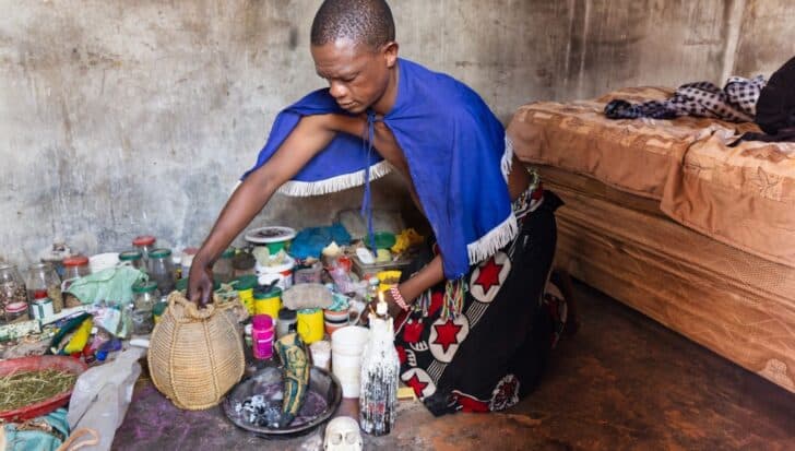 Person in traditional attire handling various objects in a setting related to African magic