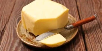 Block of butter on a rustic plate with a knife on a wooden surface