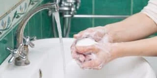 Person washing hands with a bar of soap under a running faucet