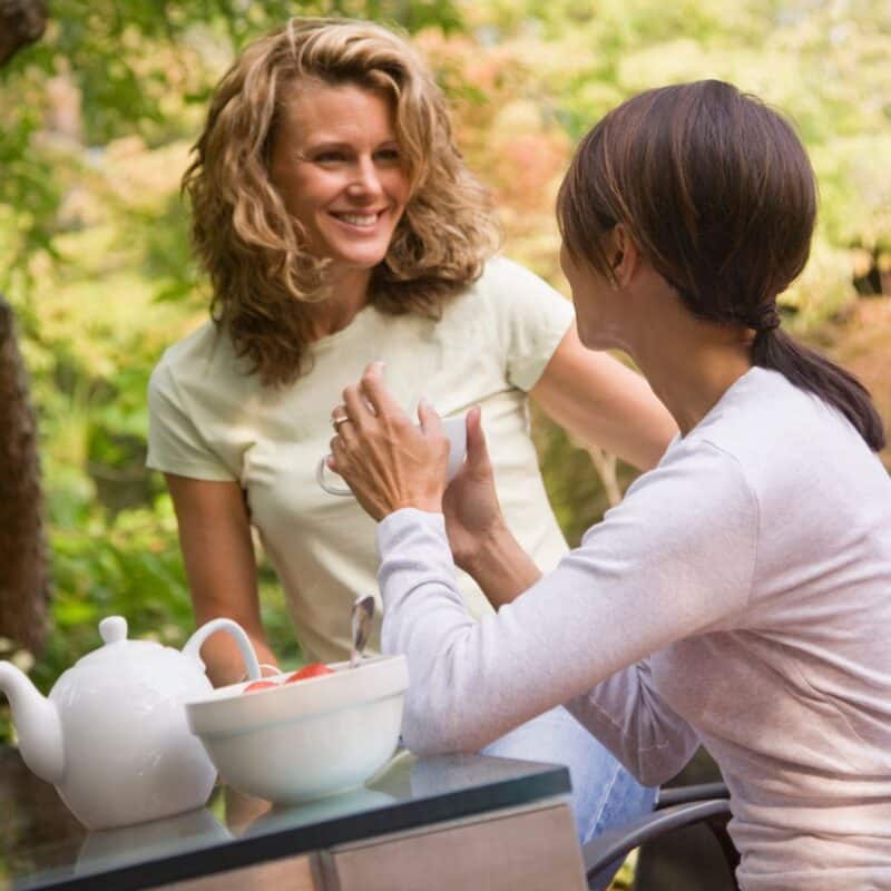 Two people engaging in a conversation outdoors with a teapot and bowl on the table