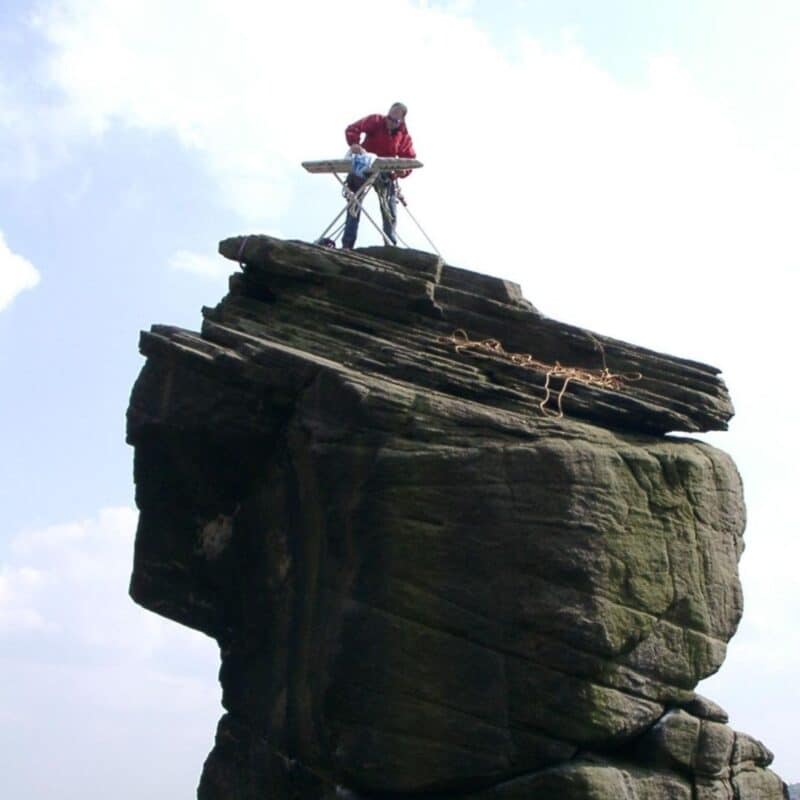 A person ironing clothes on an ironing board atop a large, rugged rock formation