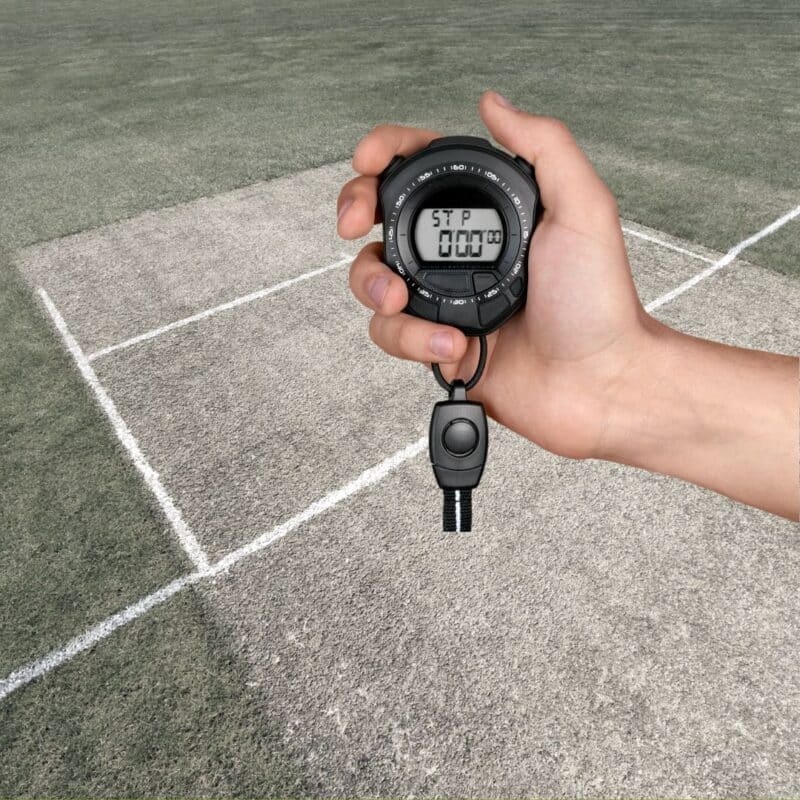 A hand holding a stopwatch on a cricket pitch boundary line