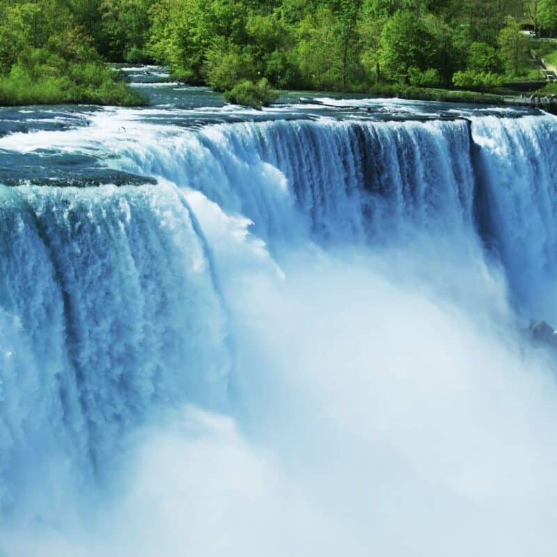 Niagara Falls with water cascading over cliffs, surrounded by lush greenery