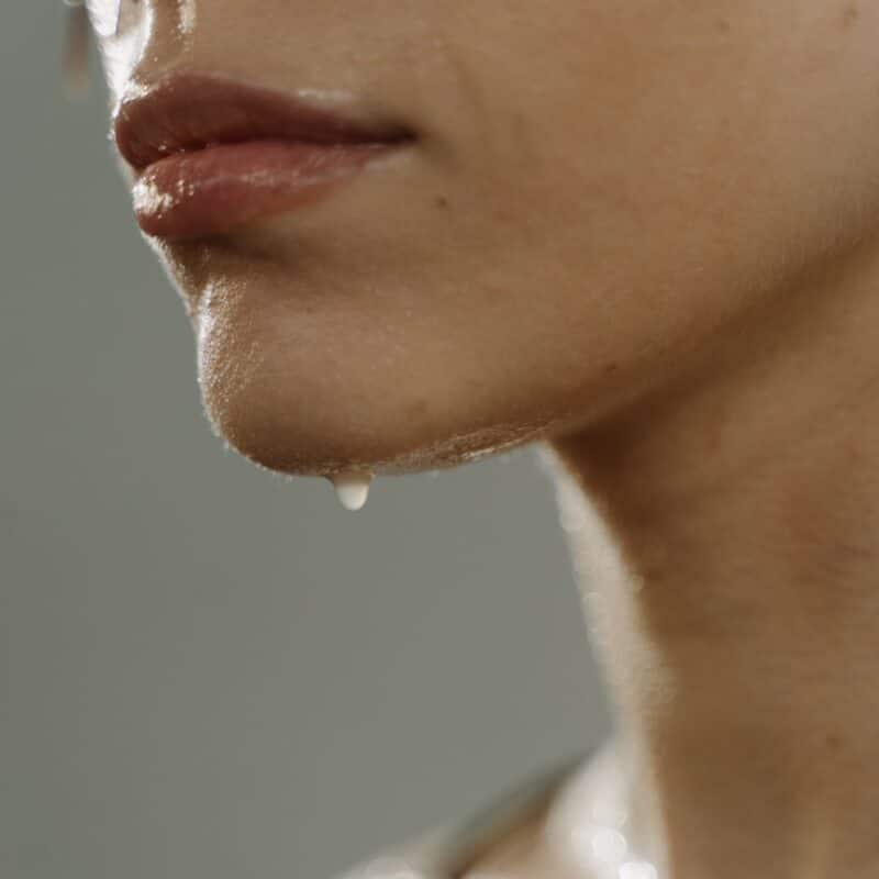 Close-up of a person's face and neck sweating, with beads of sweat dripping from their chin