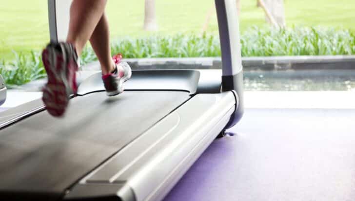 Person running on a treadmill indoors near a window overlooking green grass