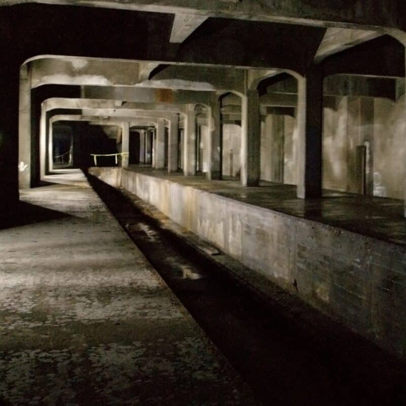 Dimly lit, unused subway tunnel with concrete pillars and a raised platform