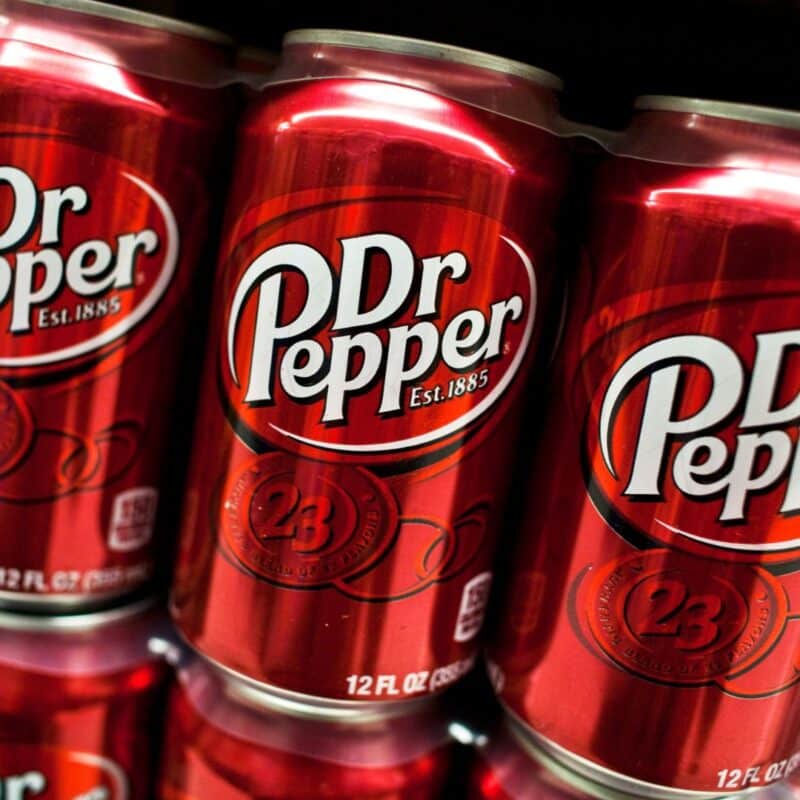 Three red cans of Dr Pepper soda featuring the modern logo