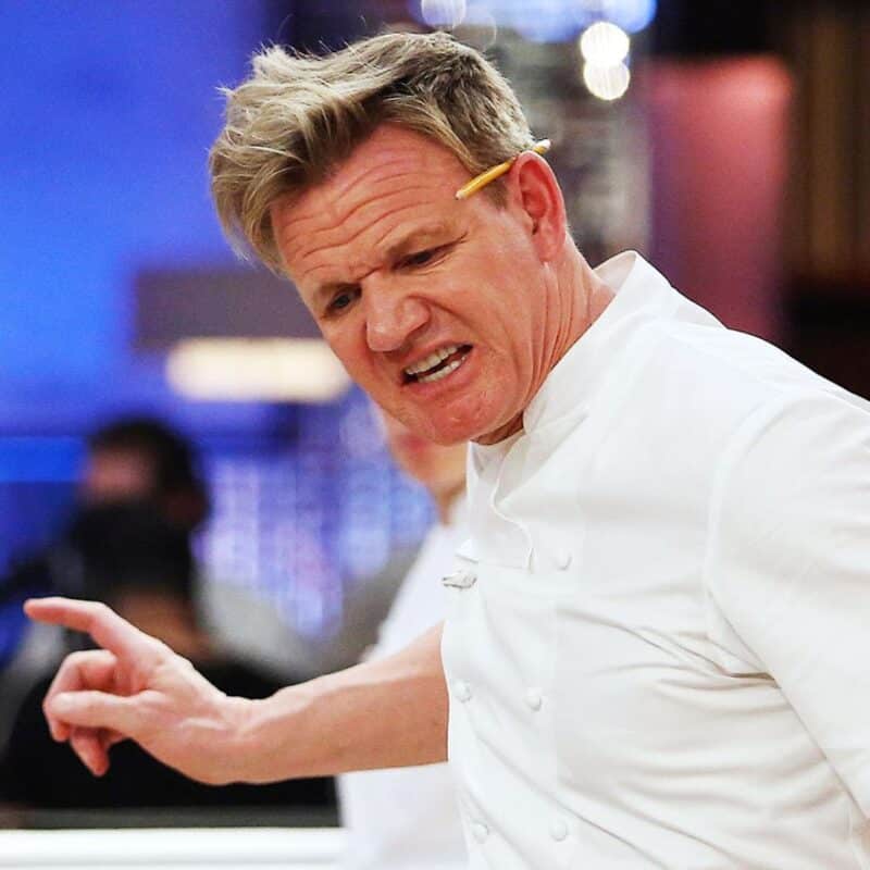 Gordon Ramsay wearing a white chef's jacket with a pencil behind his ear