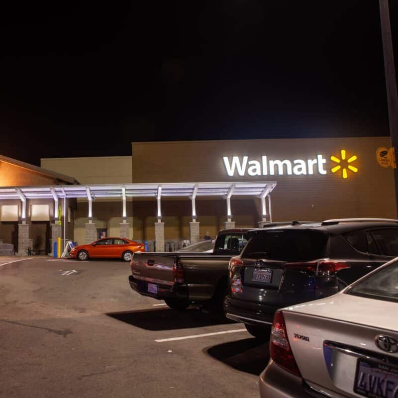 Several parked cars outside a well-lit Walmart store at night