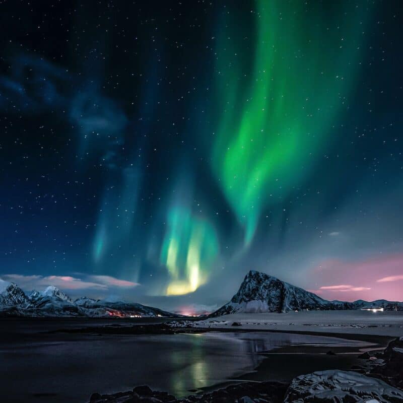 Vibrant green Northern Lights illuminate a snowy mountain landscape under a starry night sky