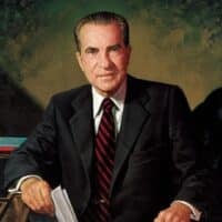 Richard Nixon sitting in a suit and tie, holding papers