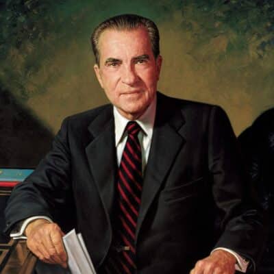 Richard Nixon sitting in a suit and tie, holding papers