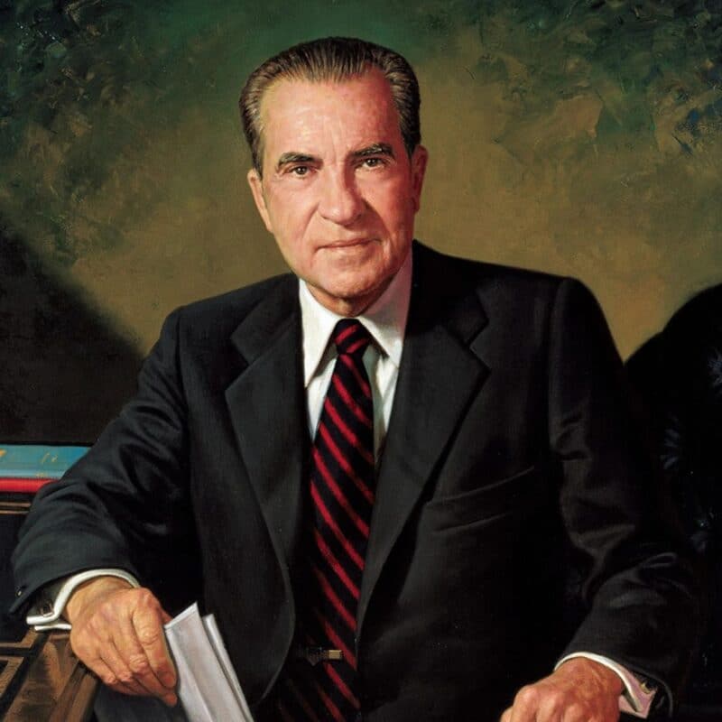 Richard Nixon sitting in a suit and tie, holding papers