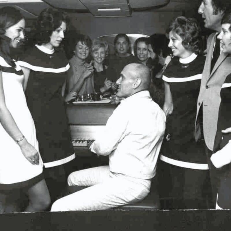 Passengers gathering around a man playing the piano in the lounge area of an airplane