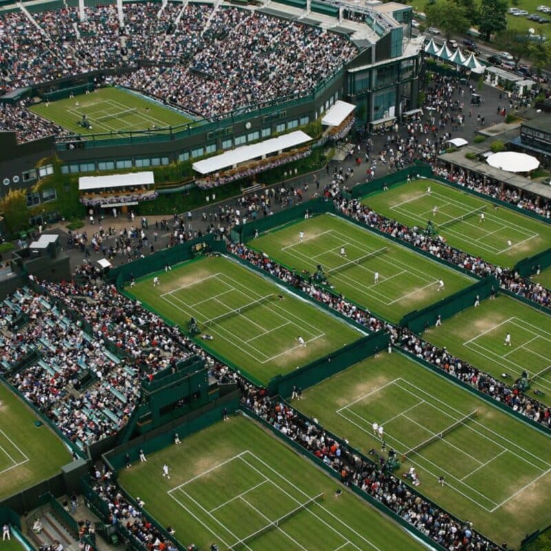 Aerial view of Wimbledon with multiple tennis courts and a large crowd of spectators