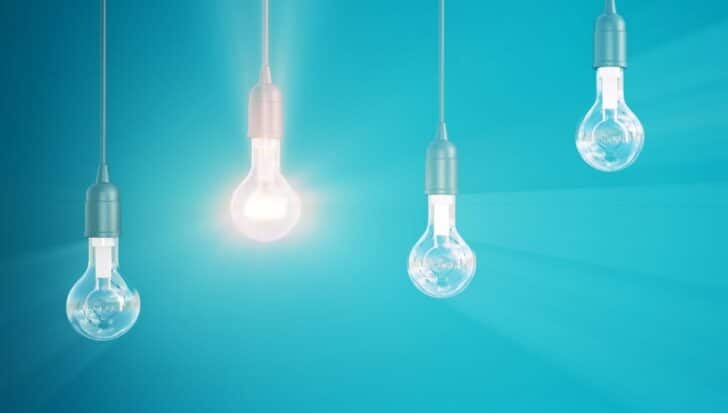 Four hanging light bulbs with one illuminated against a blue background