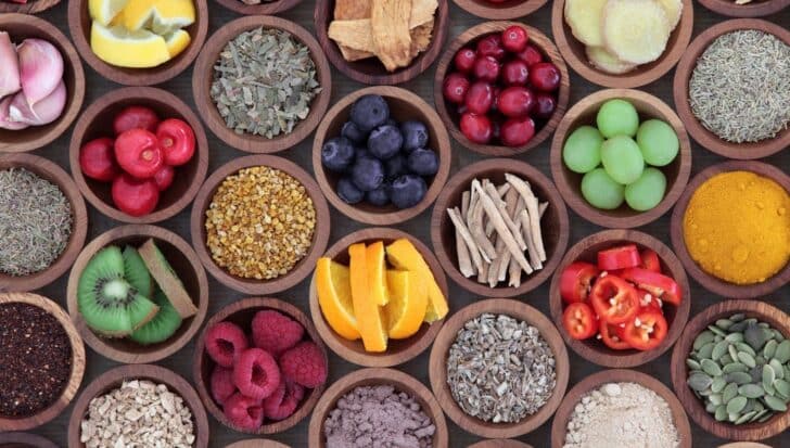 Various bowls filled with fruits, spices, and herbs such as lemon, ginger, berries, kiwi, peppers, and seeds