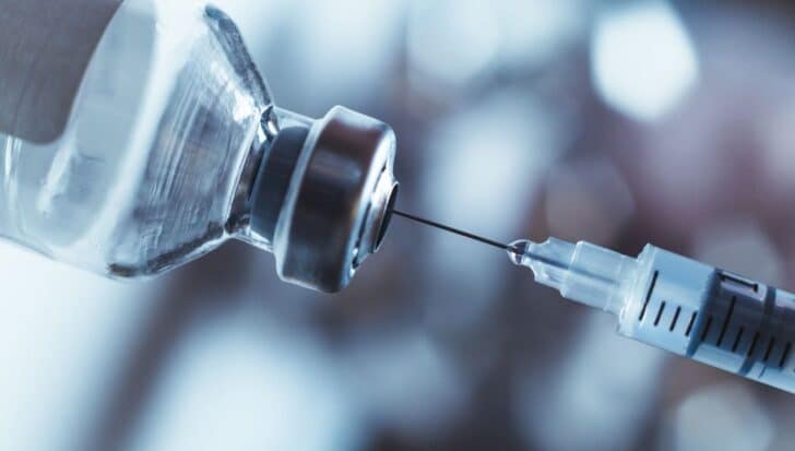 A syringe needle being inserted into a vaccine vial
