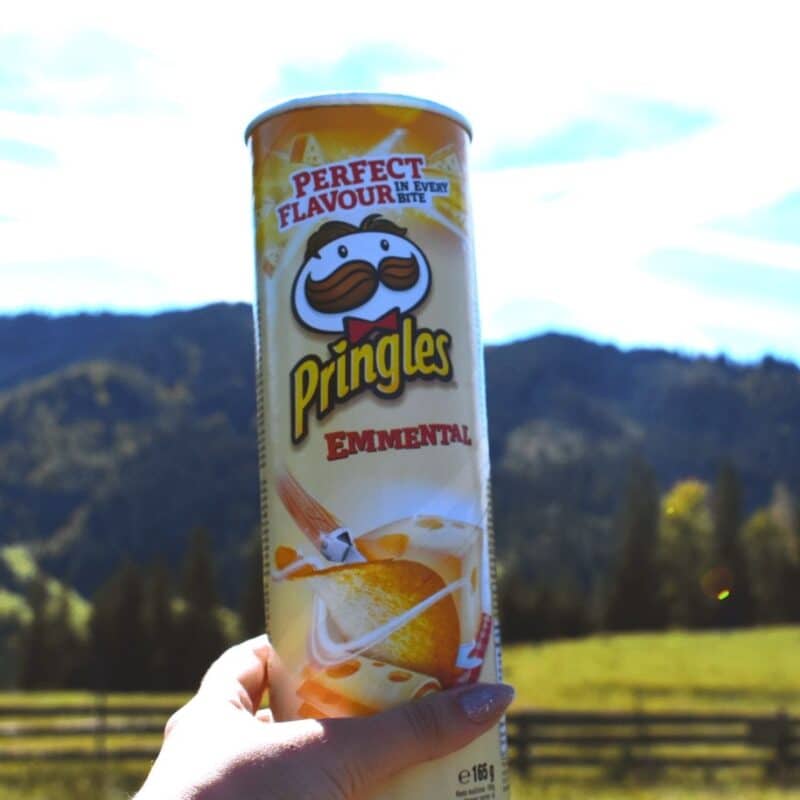 Hand holding a can of Emmental-flavored Pringles outdoors with mountains in the background
