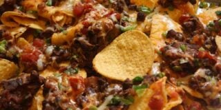 Delicious nachos topped with melted cheese, black beans, diced tomatoes, and green herbs