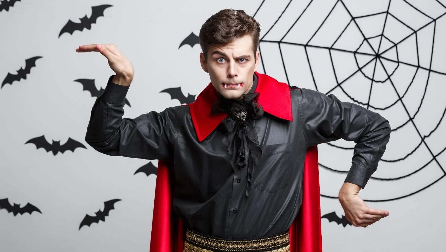 A man in a black suit and a red cape and vampire teeth in a silly pose.