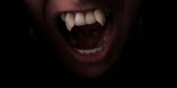 A face looming out of the darkness baring long, pointed white vampire teeth