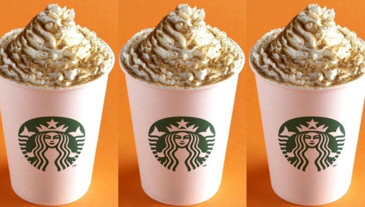 Three Starbucks cups filled with whipped cream and pumpkin spice on an orange background