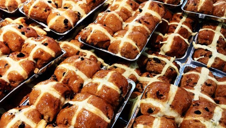 Trays of hot cross buns with raisins and a glazed topping, featuring white icing crosses
