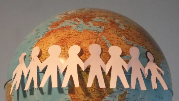 Paper cutouts of people holding hands wrapped around a globe.