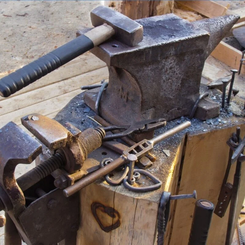 Blacksmith tools including an anvil, hammer, and vise on a wooden workbench